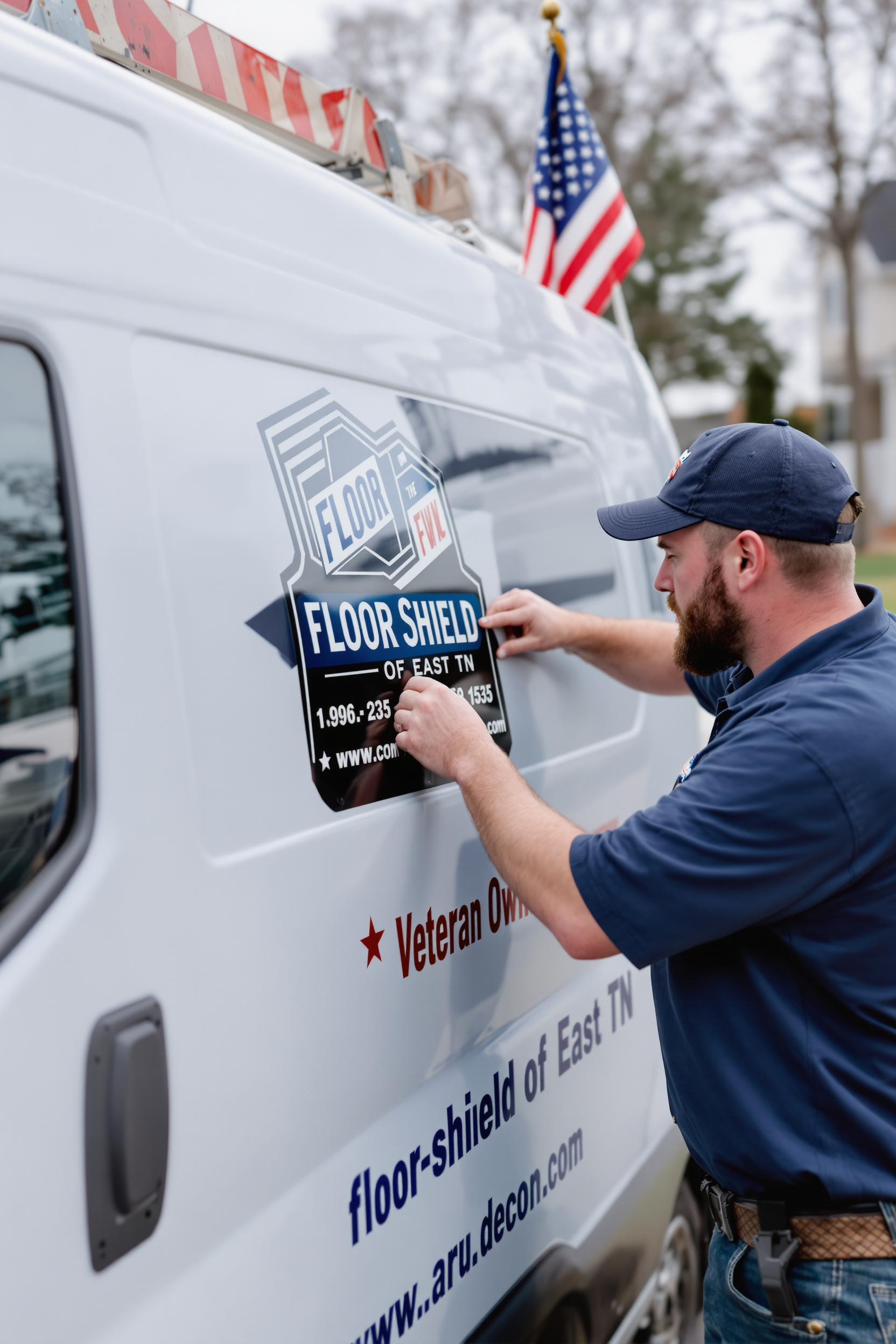 “A Floor Shield of East TN technician applying a company decal to a service van with an American flag in the background.” “A Floor Shield of East TN technician applying a company decal to a service van with an American flag in the background.”