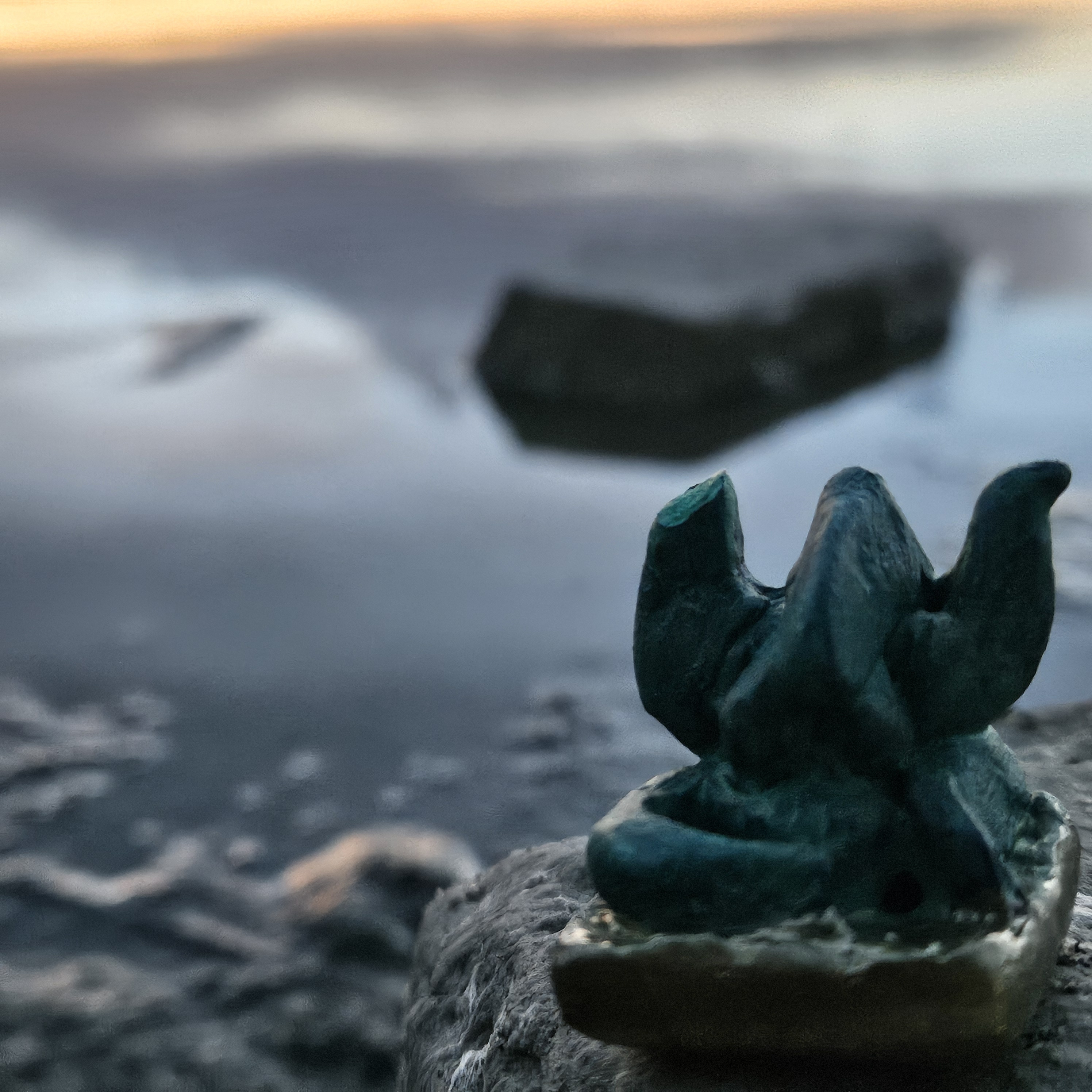 A close-up view of a small dark sculptural form by Chris Holtorf (Ombwah), positioned on a rough rock surrounded by water. The sculpture’s organic, upward-reaching shapes contrast with the cool, softly focused background, giving the image an intimate and slightly mysterious atmosphere.